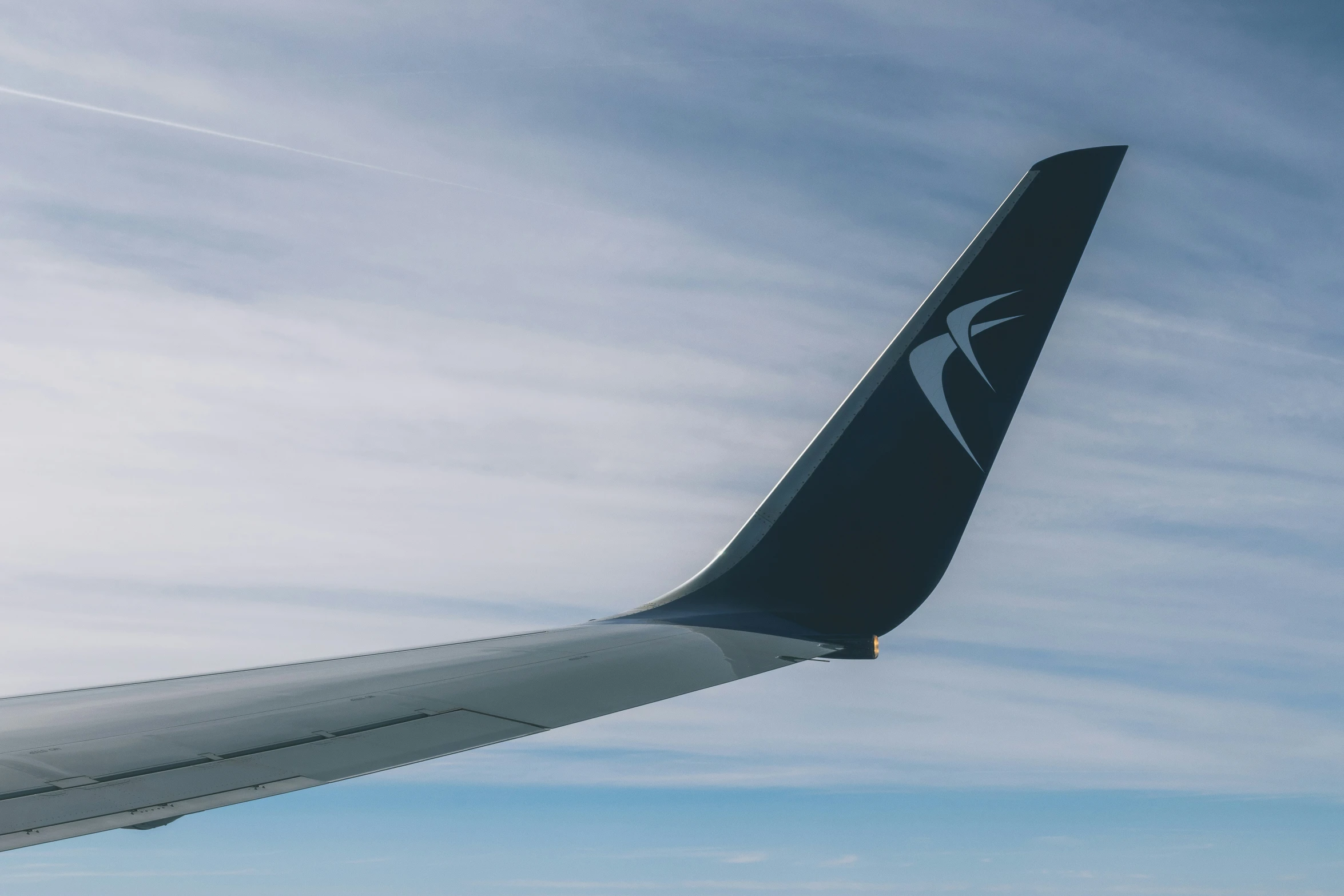 the tail end of an airplane under a partly cloudy blue sky