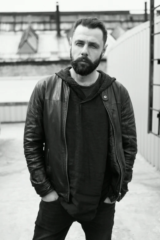 a man standing near a white wall and wearing a jacket