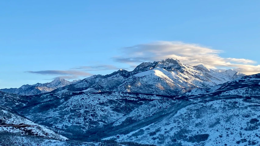 snow covered mountains under a blue sky with a light cloud