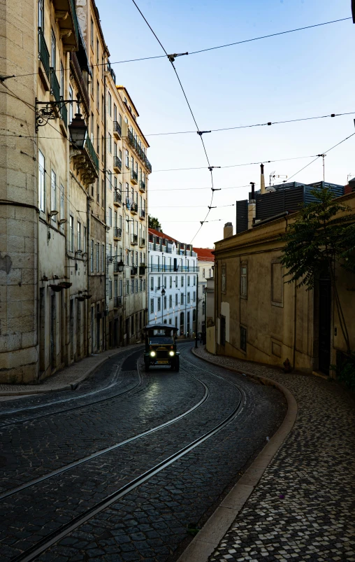 a bus moves through an alley with cobblestone road and buildings