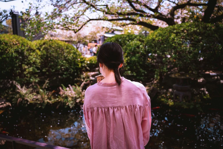 a girl in a pink shirt standing near a pond