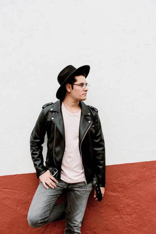 a man wearing glasses, a leather jacket and a hat