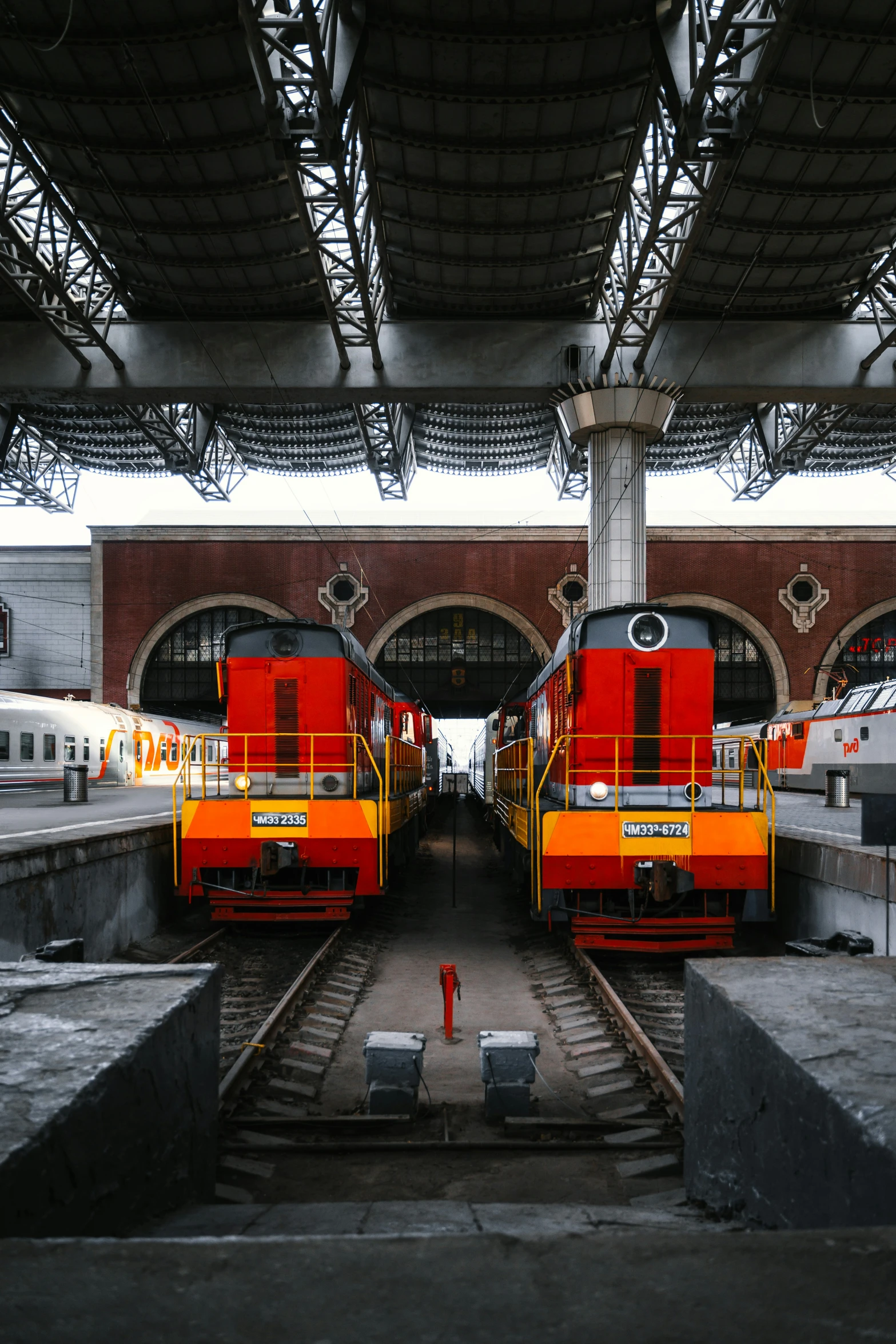 red trains in a train station are sitting in the shade