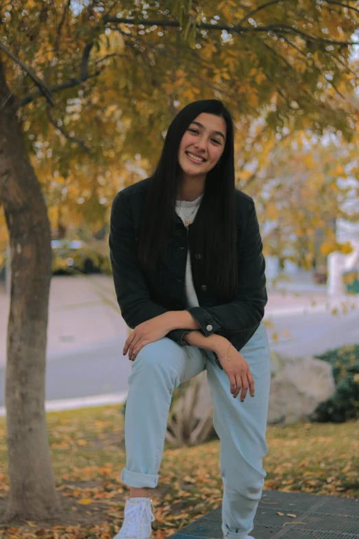 a girl sitting in front of a tree and smiling