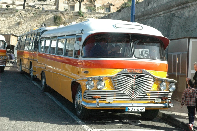 an orange and yellow bus with a woman standing next to it