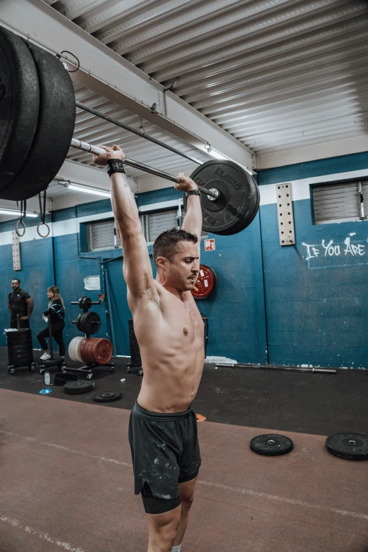 shirtless man lifting barbells in gym