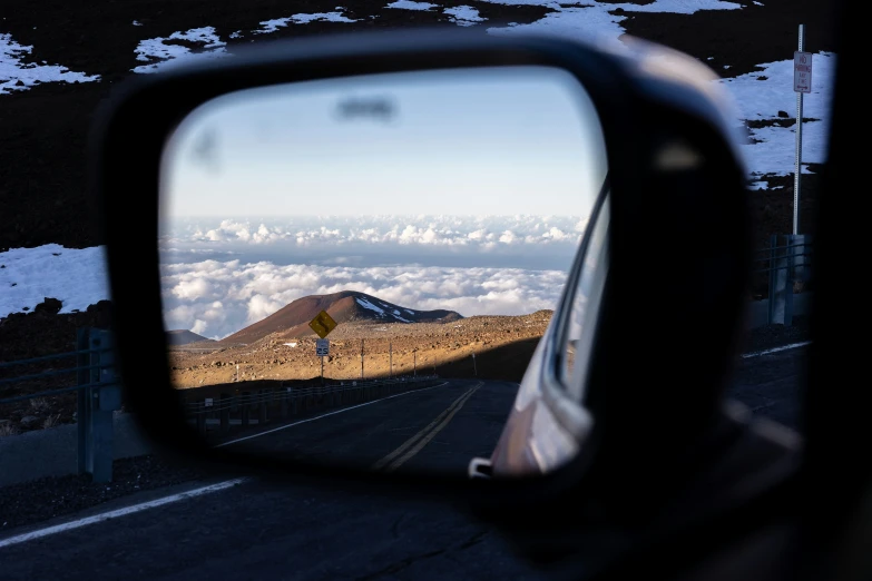 a rear view mirror showing the view of a snow covered mountain and clouds