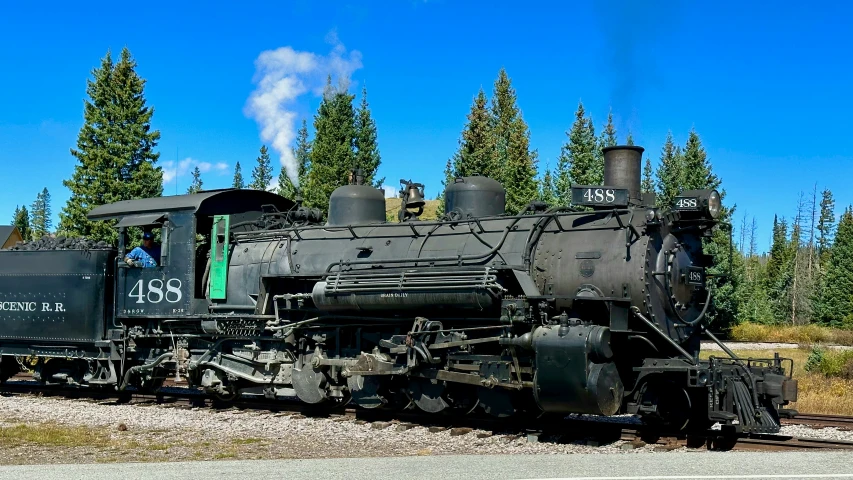 an old steam train on the tracks near some trees