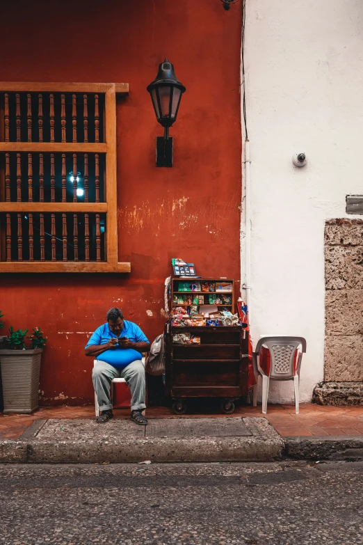 the man is sitting by himself next to his shop