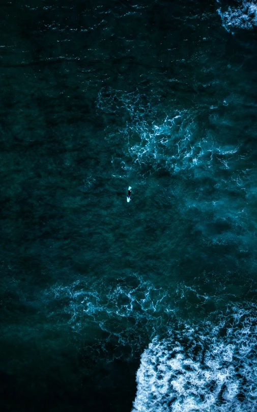 the ocean is dark and stormy as a lone surfer on a board