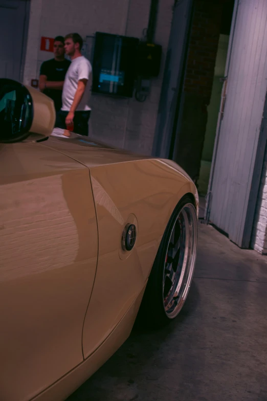 some men are hanging out in the garage next to an antique sports car