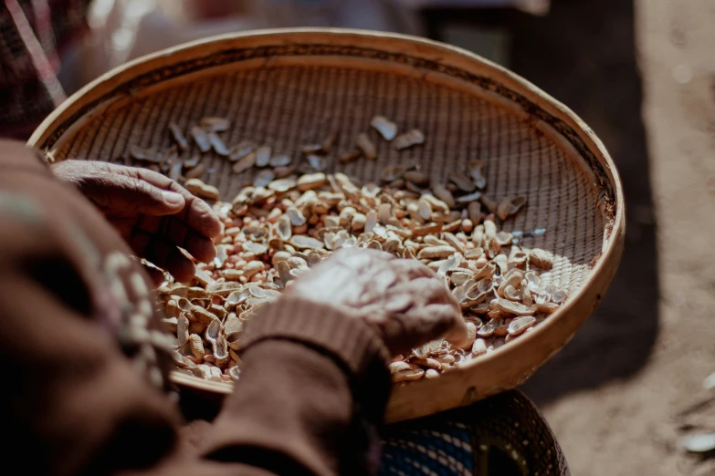 an overweight hand scoops seeds from a round, bamboo tray