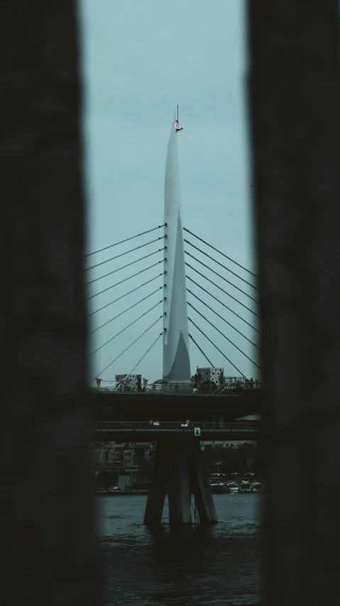 the statue sits on the bank of water with the bridge in the background