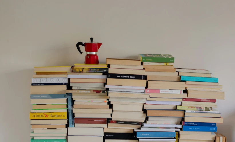 a wall of books has a red coffee mug and vase on top