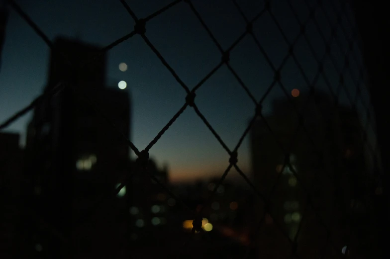 blurred night view of a building from behind a chain link fence