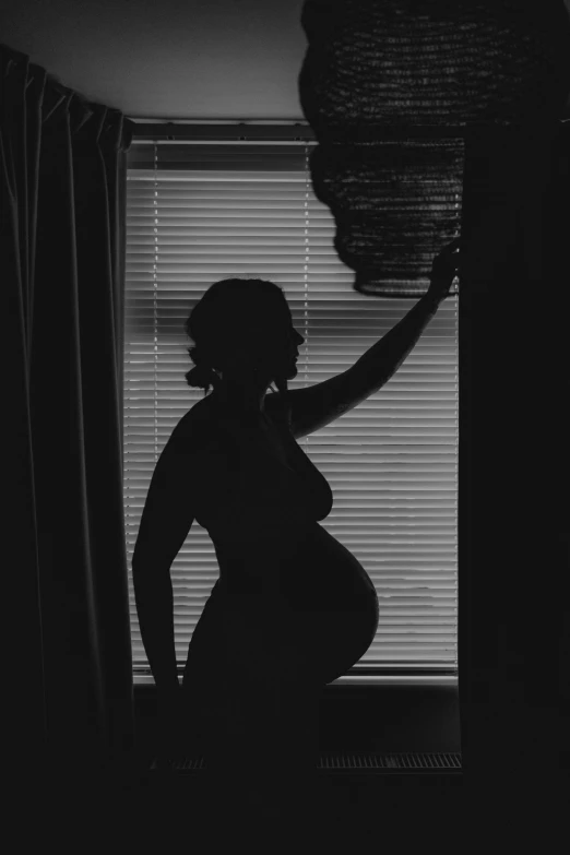 a black and white po of a pregnant woman with the shadow of the blinds