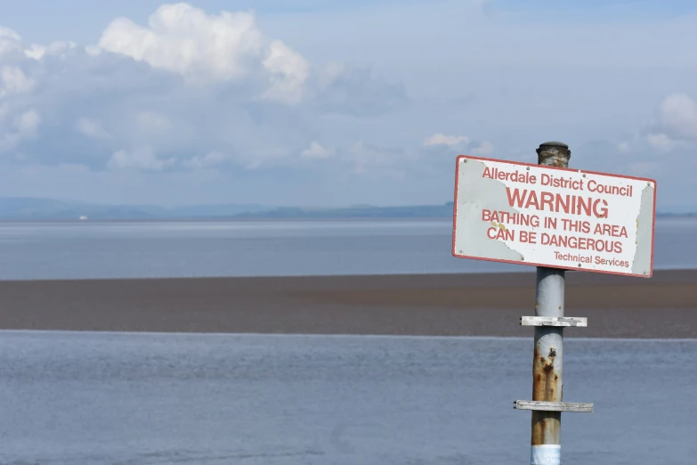 a warning sign on a metal post by the sea