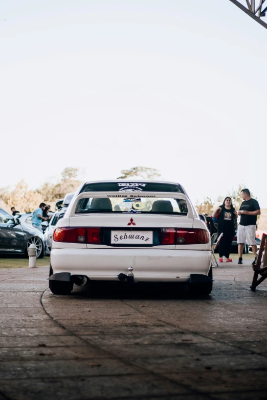 a white car parked in a lot with people walking by it