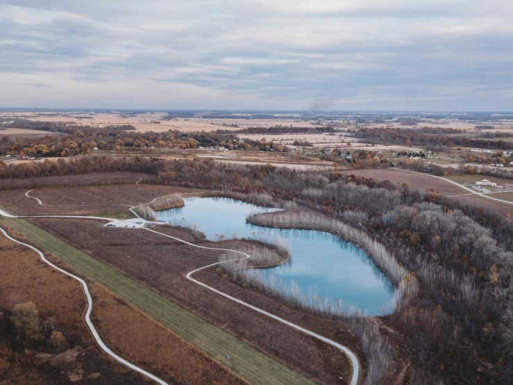 a large pond surrounded by trees in an empty field