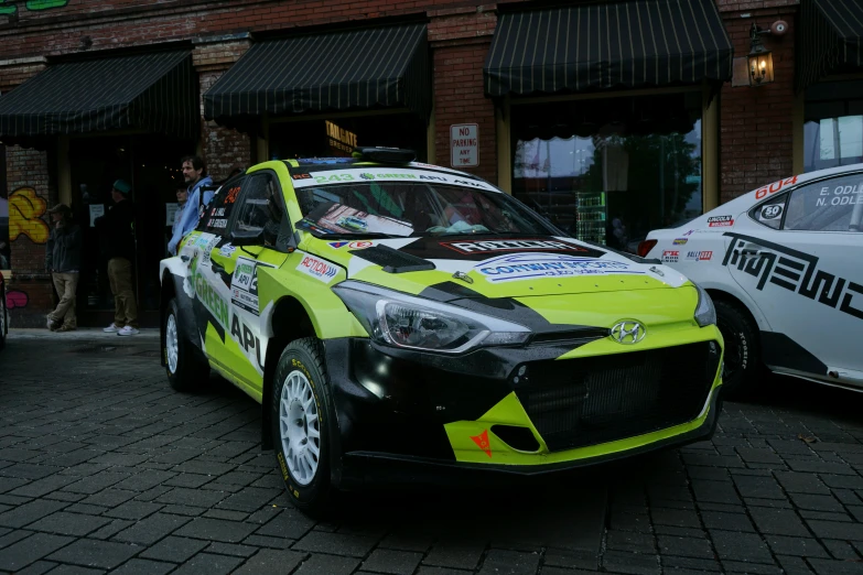 this is a yellow rally car in front of some buildings