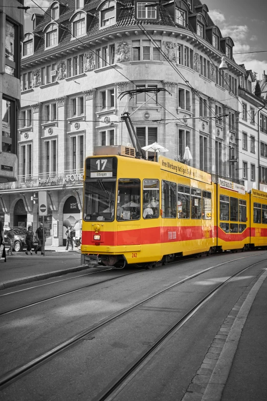 yellow tram with red stripes running past tall buildings