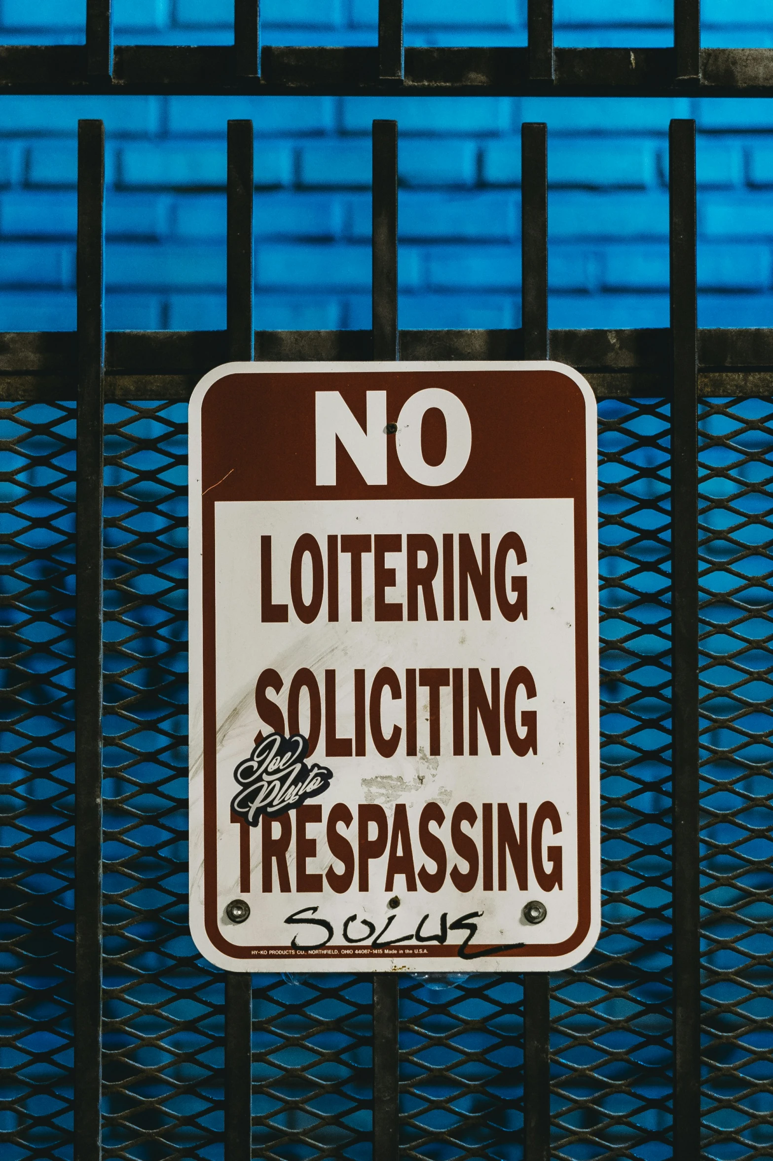 a no loitering solicing trespassing sign with a black fence