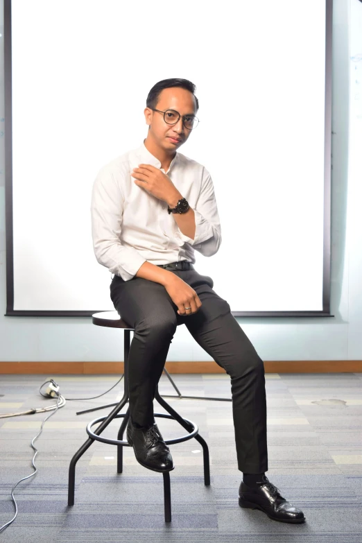 a man sits on a chair with his hands folded while holding his chest