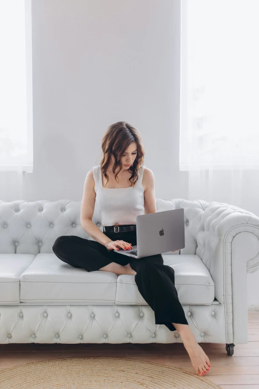 a woman sitting on top of a couch in front of a laptop computer