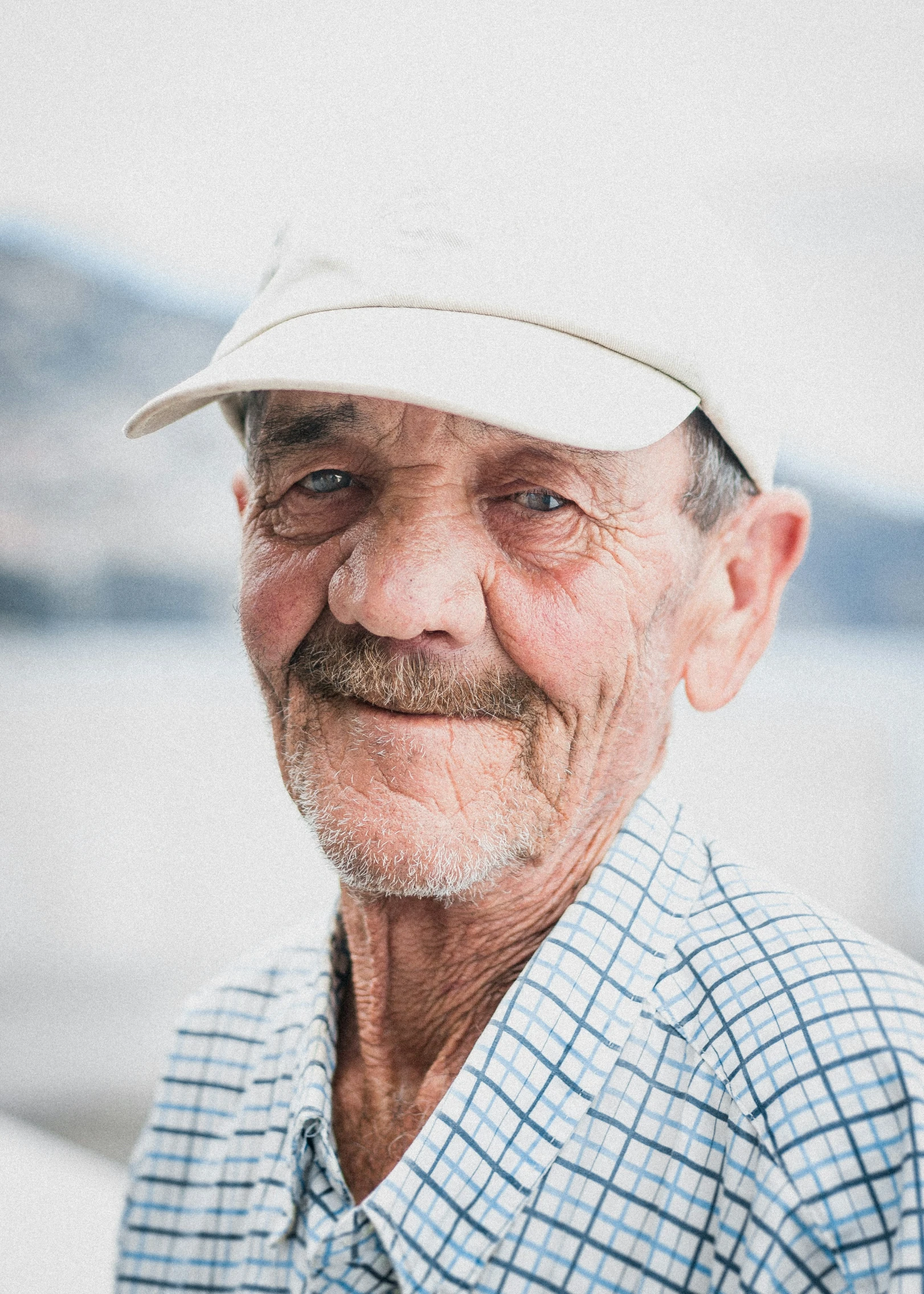 a man with a hat and plaid shirt looking into the camera