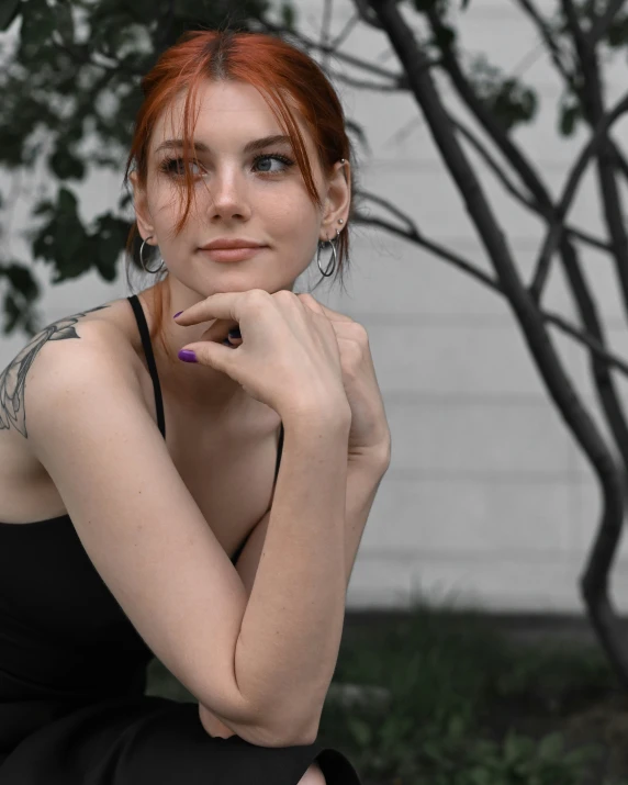 a woman in a black dress sitting in front of a tree