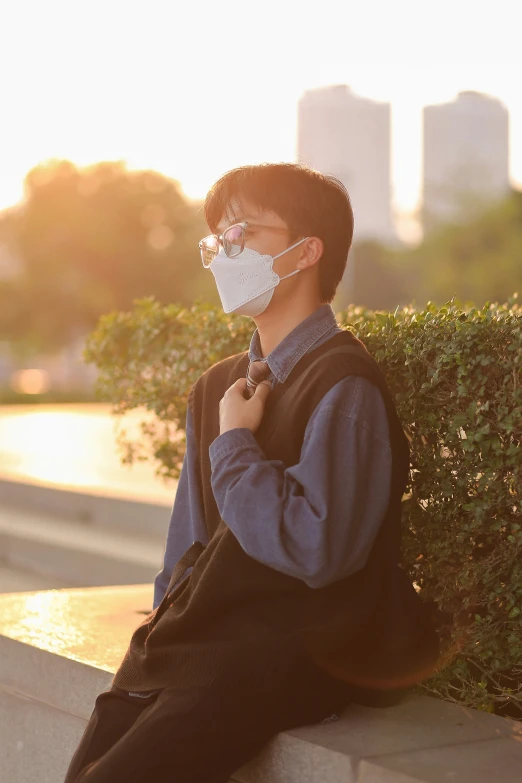 the person wearing a surgical face mask is sitting on a ledge