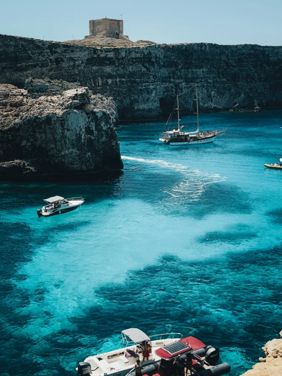 boats floating by a rocky shore with blue water