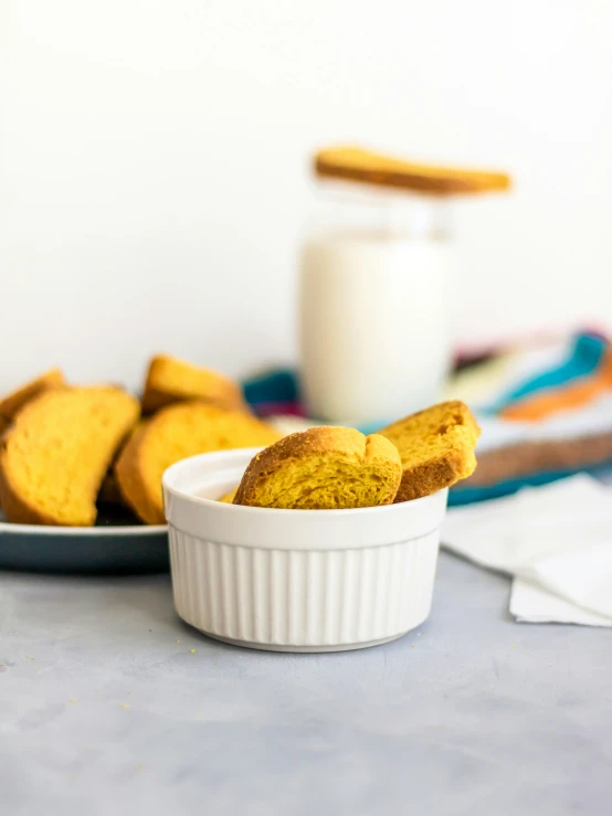 a small bowl with half eaten doughnuts next to a glass of milk