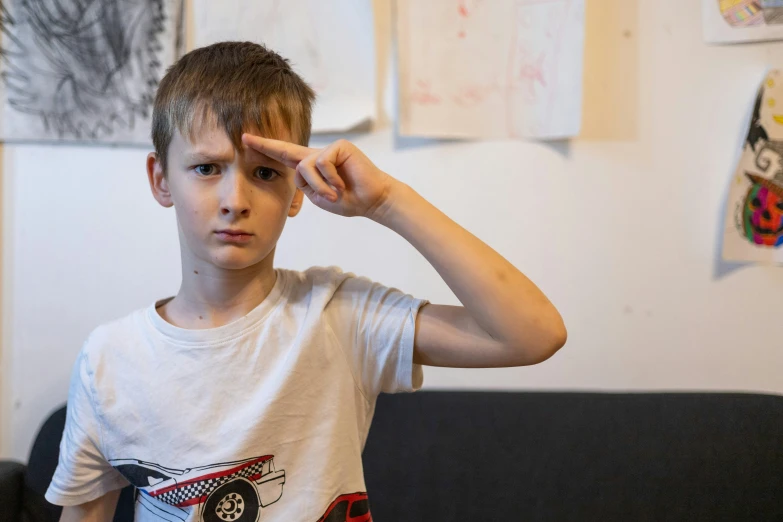 a boy in a white t - shirt is holding his hands to his head