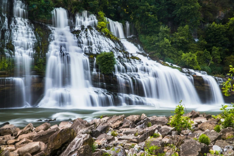 a beautiful waterfall with lots of water next to a large pile of rocks