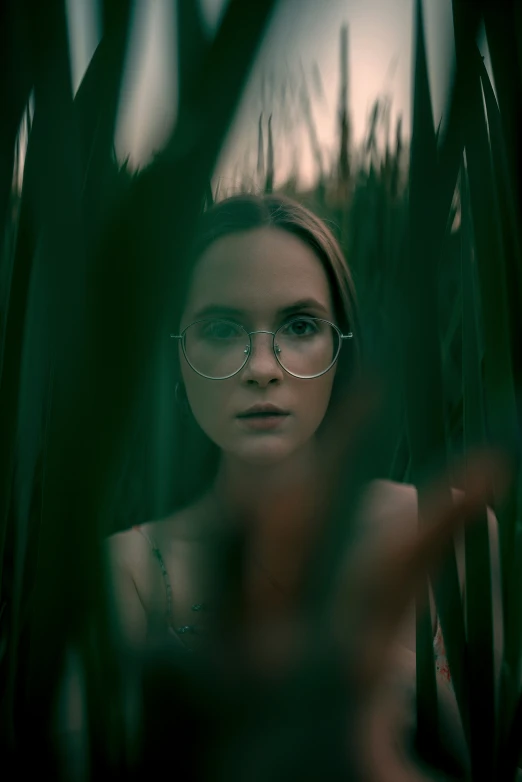 a girl wearing glasses is peeking through grass