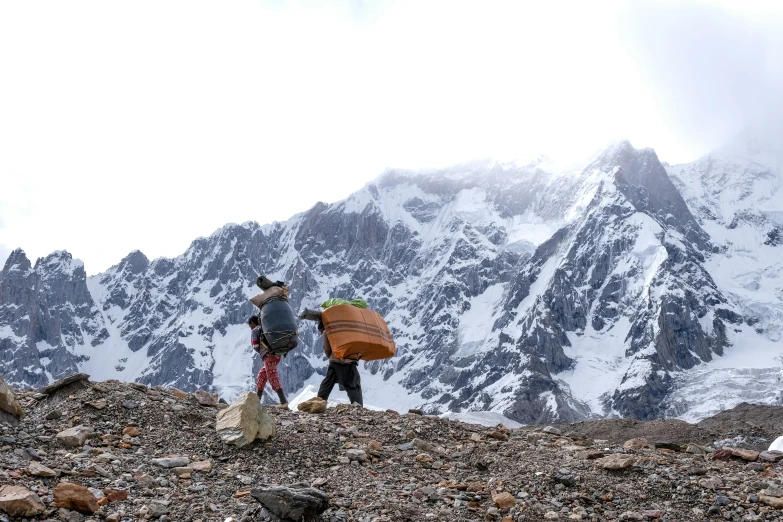 two men carrying surfboards walk up a mountain slope