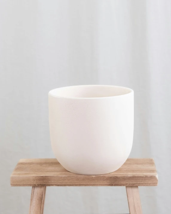 large porcelain bowl on wood stand against white wall