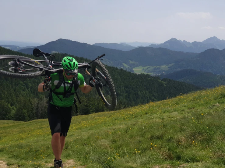 man carrying two bikes up a trail in the mountains