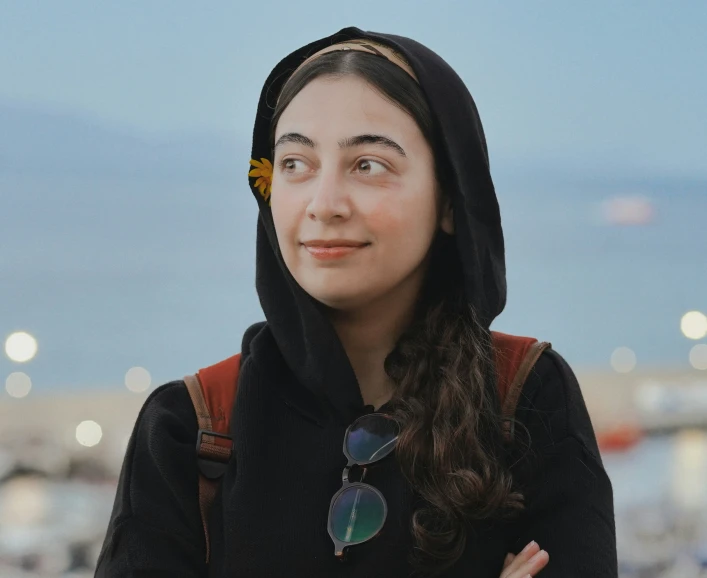 a woman standing in front of the ocean with a hood up