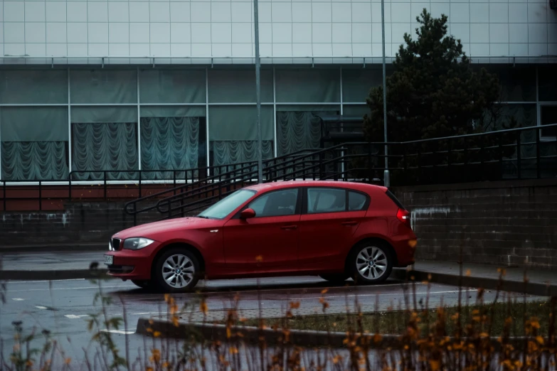 a red car is parked in the rain outside