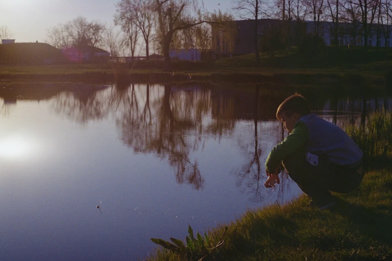 a man kneeling on the grass near water