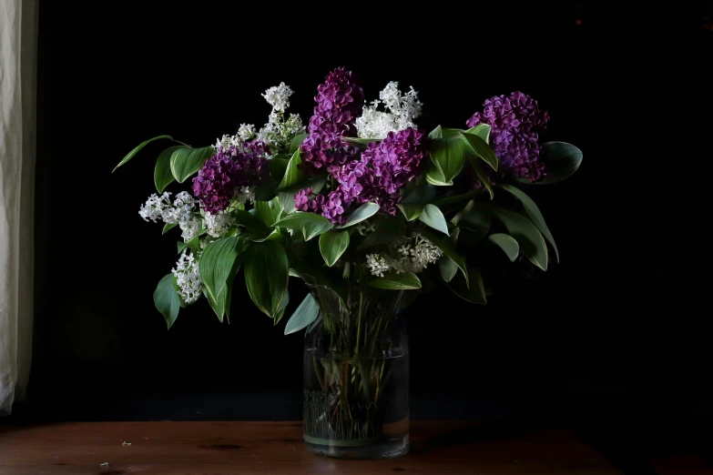 a clear vase holding purple flowers on a wooden surface