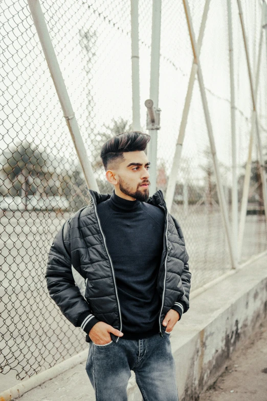 a man standing near a fence wearing black