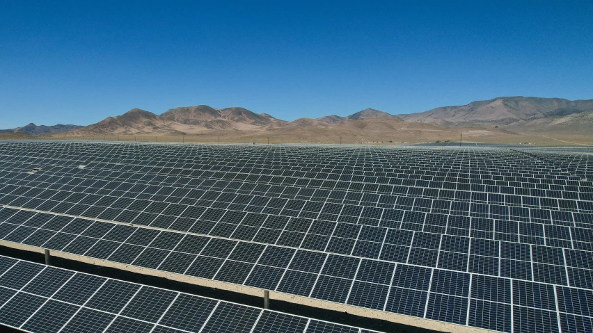 rows of rows of solar panels in front of mountains