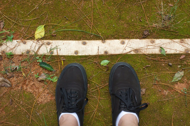 a persons legs with black tennis shoes on a grass area