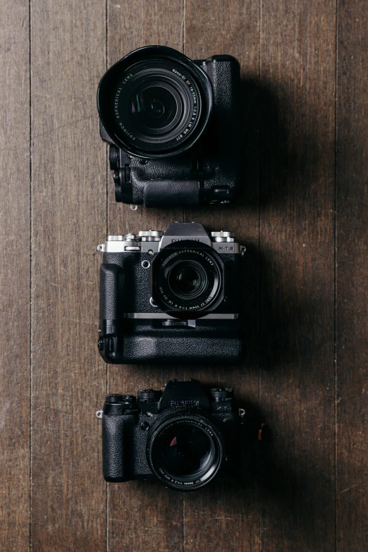 two old camera sitting side by side on top of a wood table