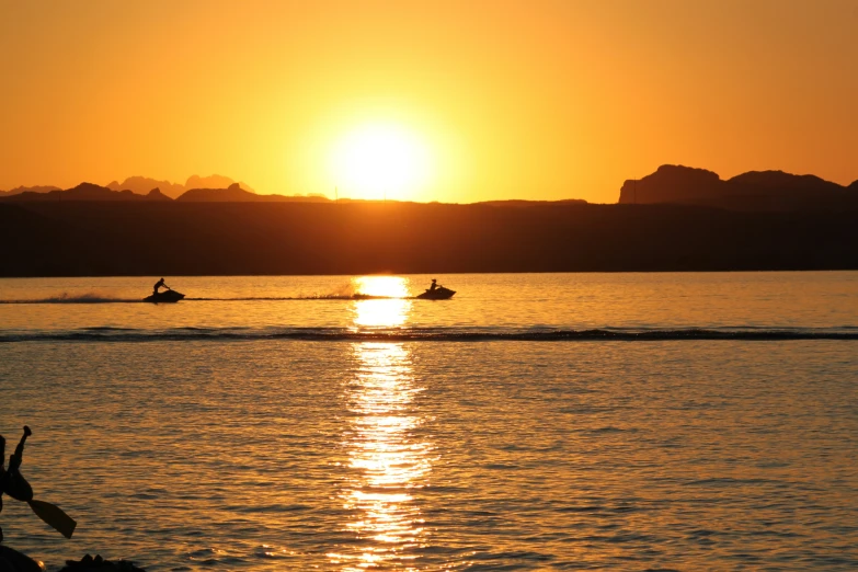 two people on jet skis are on the water as the sun sets