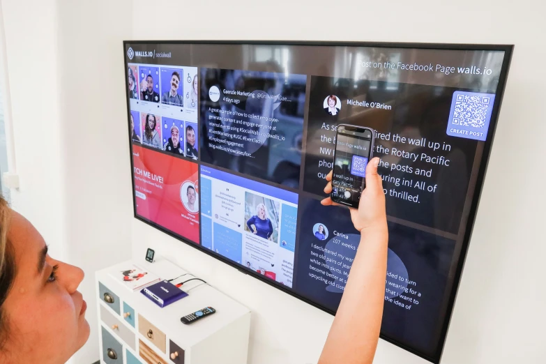 a woman taking a po of a wall mounted tv screen