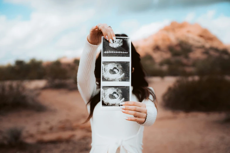 a woman holds up two polaroid prints in the desert